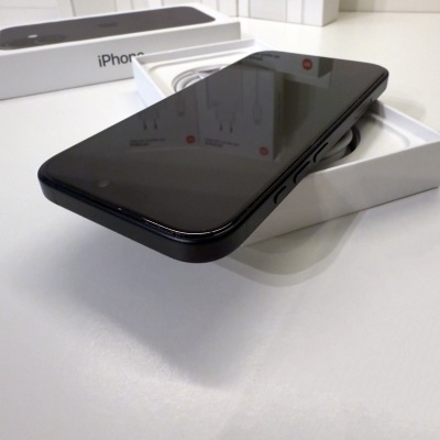 Smartphone iPhone preto dentro da caixa branco com texto iPhone em fundo de caixas com imagens de carregadores.