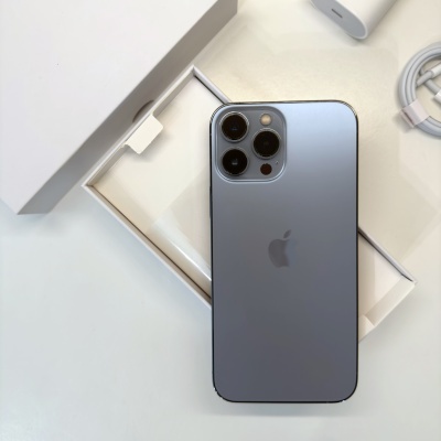 Telemóvel Apple iPhone cinza com três câmaras sobre caixa branca e acessórios.