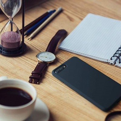 Mesa de madeira com ampulheta, lápis, relógio, telemóvel, caderno e chávena de café