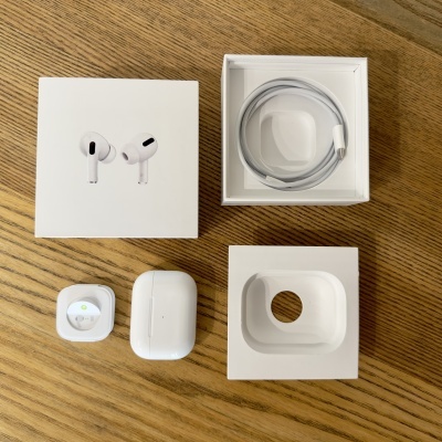 Auscultadores tipo AirPods brancos com caixa, cabo e embalagem sobre madeira.