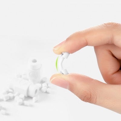 Dispositivo branco com arco verde segurado entre dedos, fundo branco com outros dispositivos semelhantes desfocados