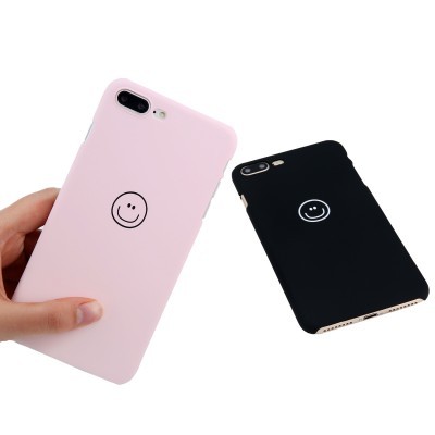 Duas capas para smartphone, uma rosa claro segurada e outra preta ao lado, ambas com símbolo de sorriso