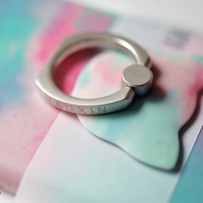 Anel prateado com gravação NAOXIN sobre papel colorido pastel