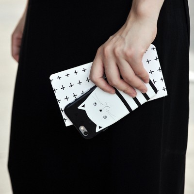 Carteira branca com padrão de cruzes pretas e telemóvel com capa de gato preto e branco na mão