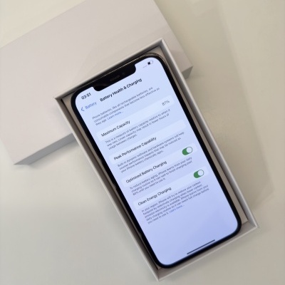 Smartphone preto dentro de caixa branca com ecrã ligado mostrando informações de bateria