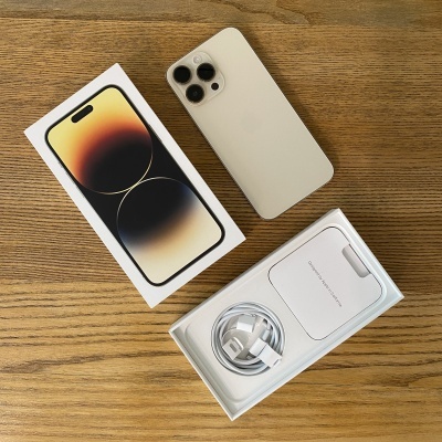 Telemóvel cinza com três câmaras, caixa e acessórios sobre mesa de madeira