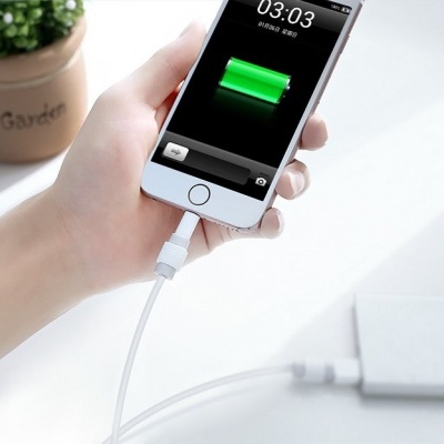 Smartphone branco a carregar ligado a power bank branca sobre mesa branca com vaso de planta ao fundo