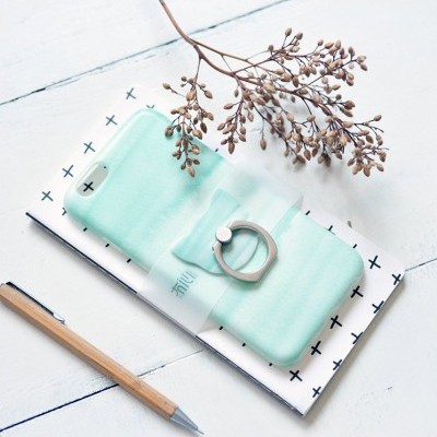 Capa de telemóvel verde água com suporte circular, bloco de notas branco com padrão de cruz preta, lápis de madeira e ramo seco