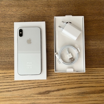 iPhone branco com caixa aberta, adaptador de energia e cabo USB em superfície de madeira.