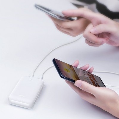 Carregador portátil branco a carregar dois telemóveis pretos em mãos sobre superfície branca