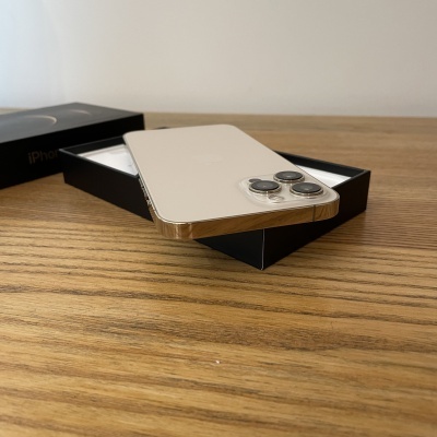 Smartphone iPhone dourado com três câmaras traseiras na caixa preta sobre mesa de madeira