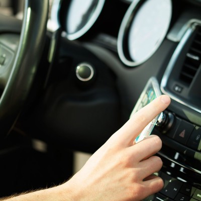 Mão a tocar no ecrã de um sistema de navegação num painel de carro preto e cinza