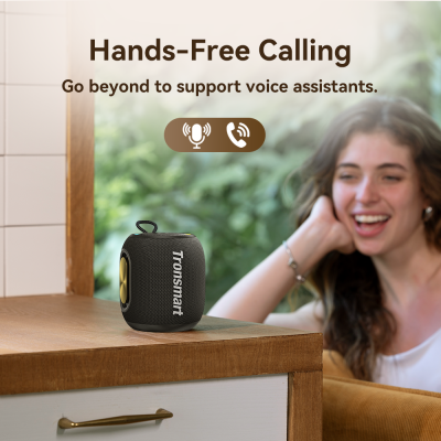 Coluna portátil preta Tronsmart com detalhes dourados numa mesa de madeira.