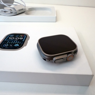 Relógio inteligente cinza na embalagem branca com imagem do ecrã às 10:09 e carregador branco ao fundo