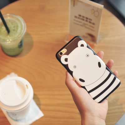 Telemóvel com capa decorativa de hipopótamo sobre mesa com copos de bebidas