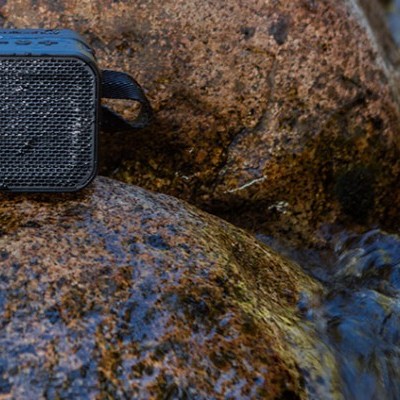 Coluna sonora portátil preta sobre pedras ao lado de água