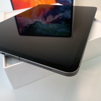 Tablet preto com ecrã brilhante refletindo cores, sobre caixa branca