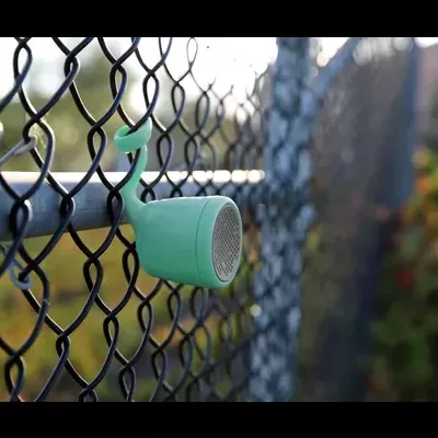 Coluna portátil verde pendurada numa vedação metálica azul