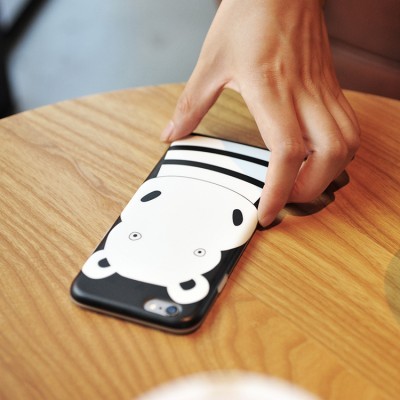 Telemóvel com capa branca e desenho de urso preto sobre mesa de madeira.