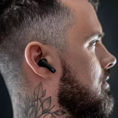 Auricular preto intra-auricular no ouvido de homem com barba, tatuagem no pescoço e cabelo curto