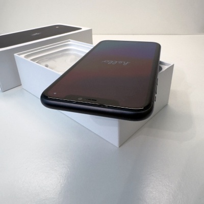 Smartphone preto em cima de uma caixa branca aberta sobre uma superfície branca.