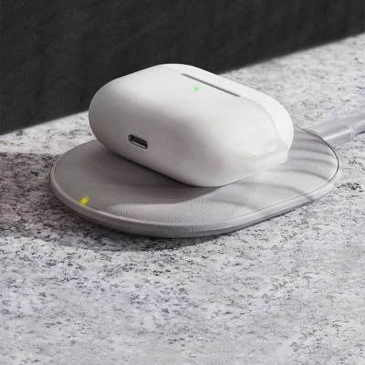 Carregador sem fios cinza com caixa de auscultadores brancos em cima sobre superfície de pedra