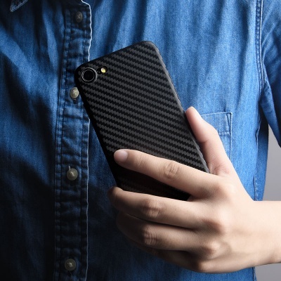 Mão segura smartphone com capa preta texturizada, pessoa de camisa azul ao fundo