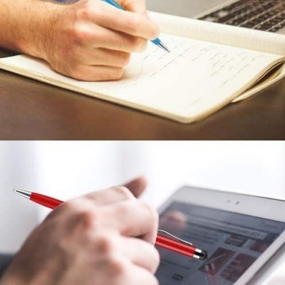 Pessoa escrevendo num caderno com caneta azul e outra mão usando caneta vermelha num tablet