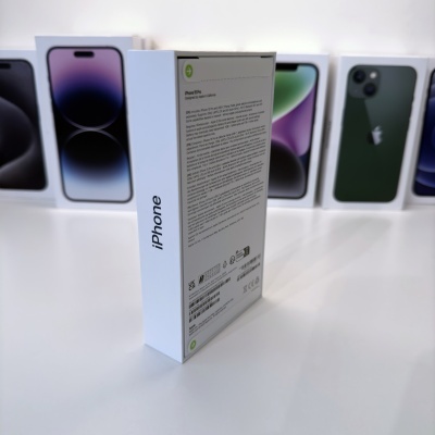 Caixa branca de iPhone com texto impresso, cercada por várias caixas de iPhones coloridos sobre superfície branca