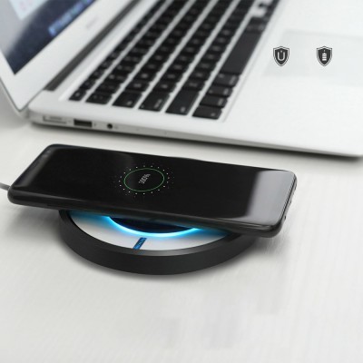 Carregador sem fios preto redondo a carregar smartphone próximo de portátil prateado