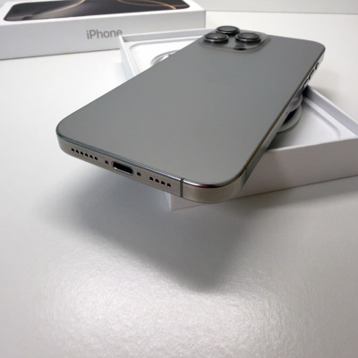 Smartphone iPhone cinzento com três câmaras atrás numa caixa branca com a palavra iPhone em fundo branco.