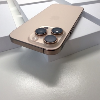 Smartphone dourado com três câmeras numa disposição triangular sobre caixas brancas.