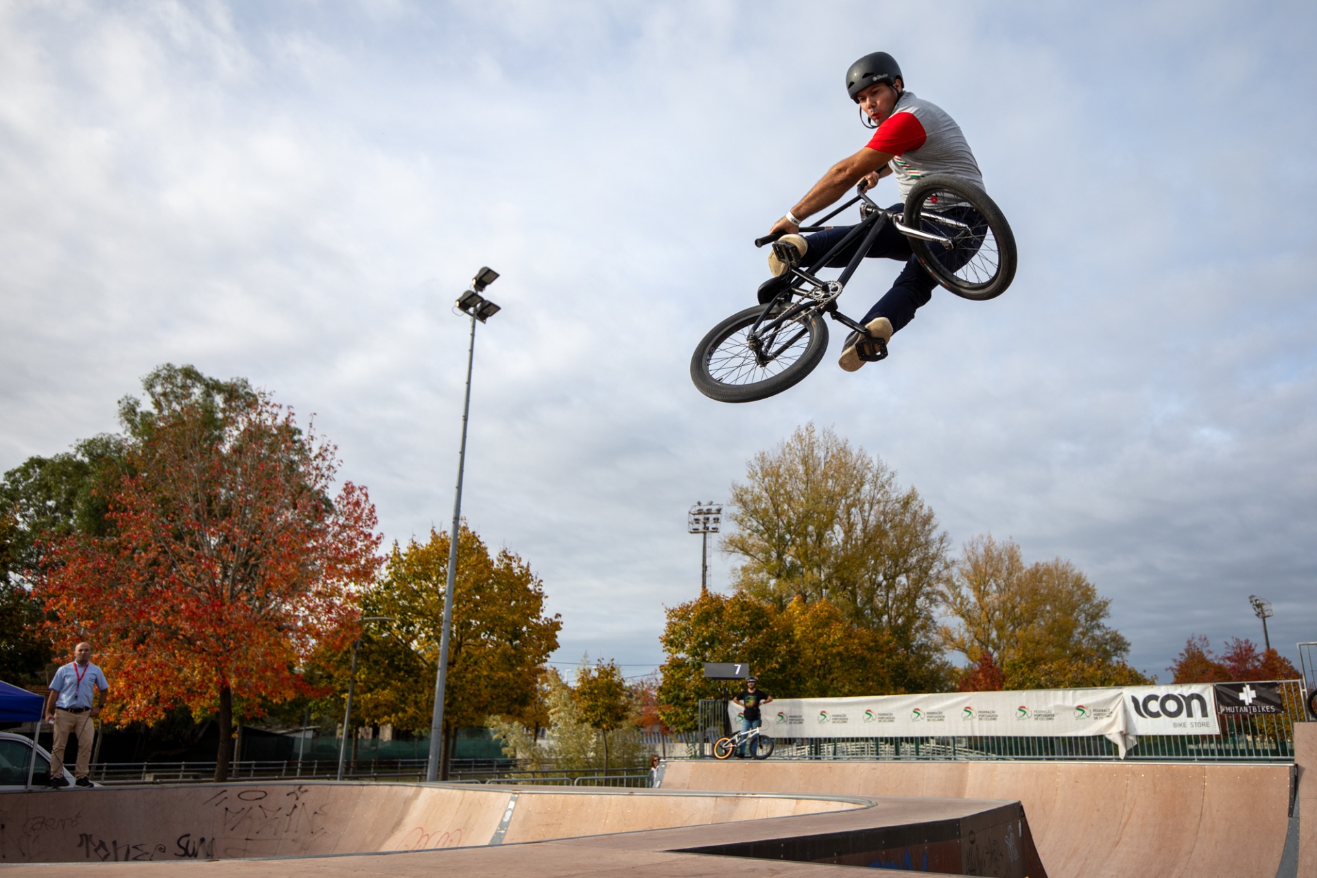 Jovem a fazer manobra aérea numa bicicleta BMX preta num parque de skate ao ar livre no outono