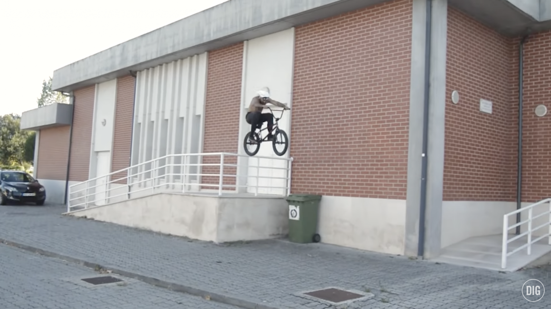 Pessoa de bicicleta BMX a saltar corrimão branco perto de muro de tijolos