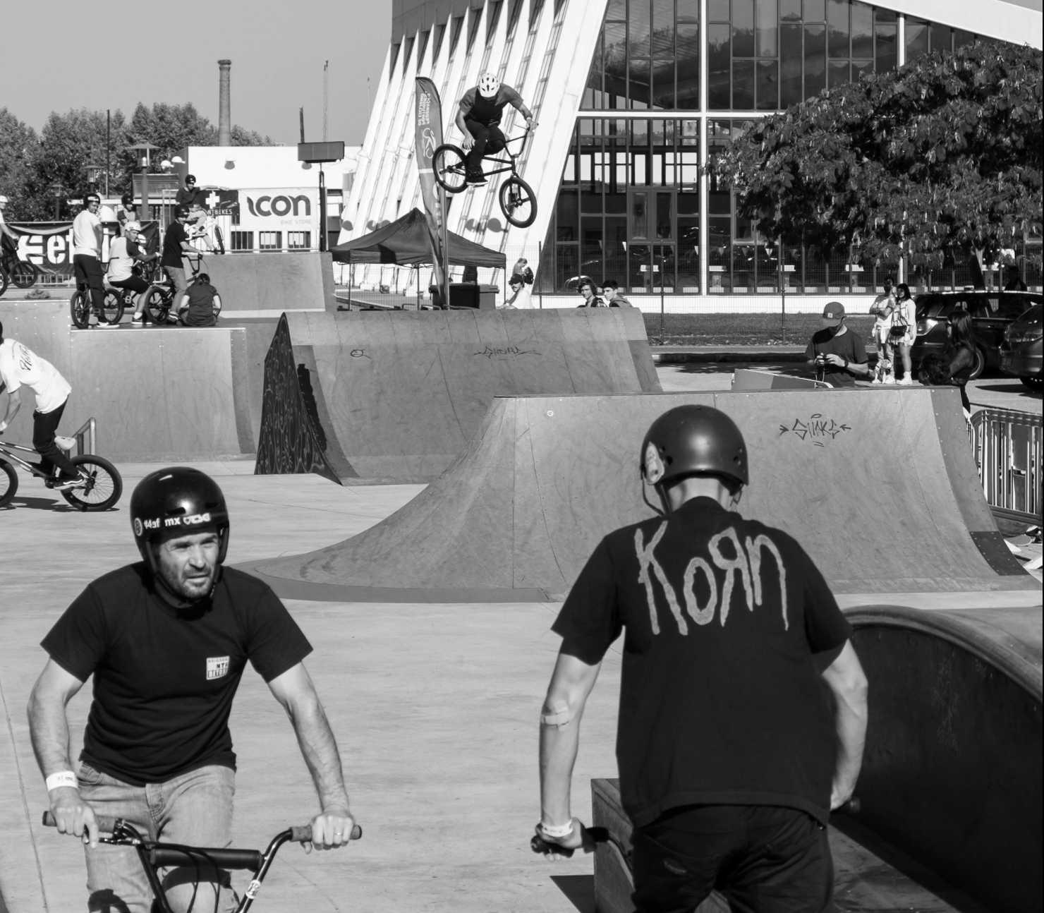 Parque de skate em preto e branco com rampas e pessoas a andar de bicicleta BMX.