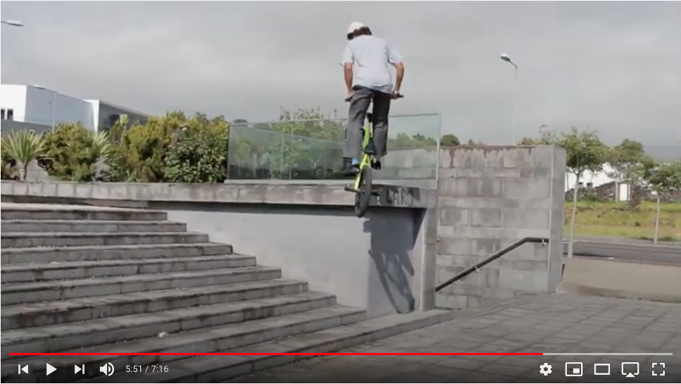 Pessoa numa trotinetta preta a saltar de um corrimão em escadas urbanas de cimento.