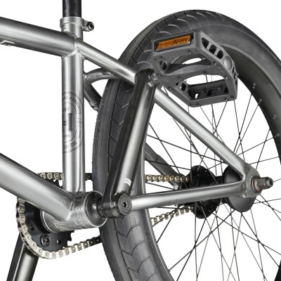 Parte traseira de bicicleta com quadro metálico cinza, pedal preto e roda preta