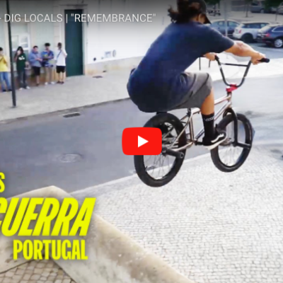 Jovem em bicicleta BMX a saltar na calçada portuguesa com pessoas ao fundo
