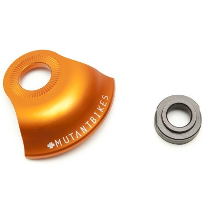 Peça metálica alaranjada com inscrição MUTANTBIKES e rolamento de metal ao lado sobre fundo branco