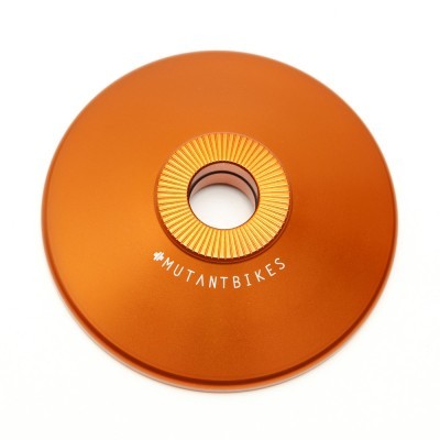 Peça circular metálica laranja com anel central texturizado e texto #MUTANTBIKES.