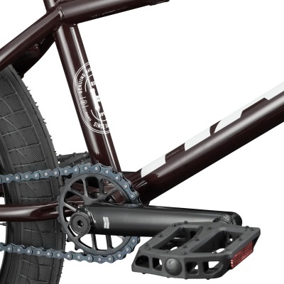 Pedaleira, corrente e quadro de bicicleta BMX castanho escuro com texto branco e pedal preto com refletor.