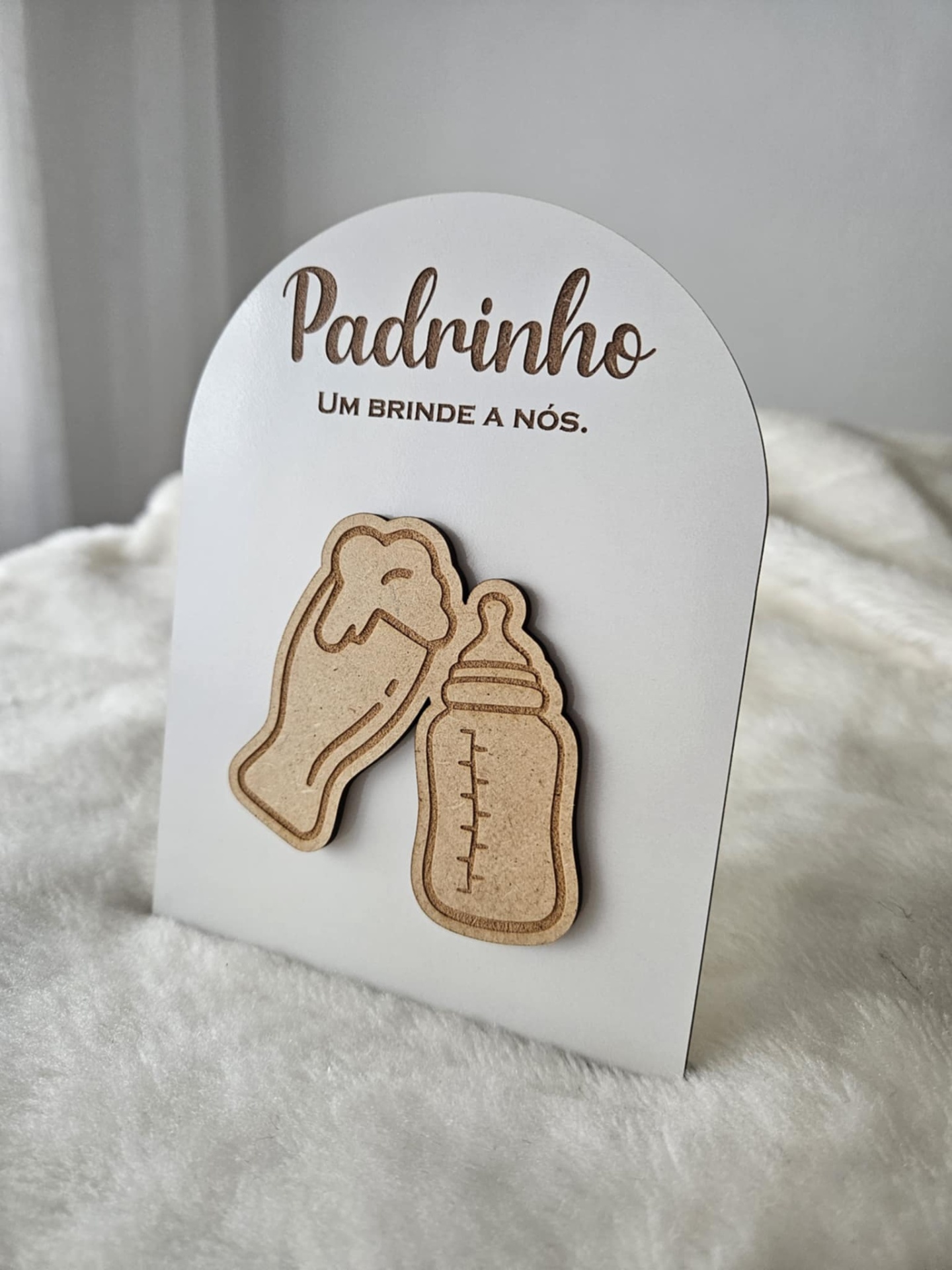 Expositor para prendas com mensagem para padrinho e ímanes de madeira de copo de cerveja e biberão sobre tecido branco.