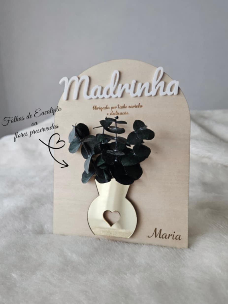 Placa decorativa de madeira com vaso dourado, folhas preservadas e texto para madrinha