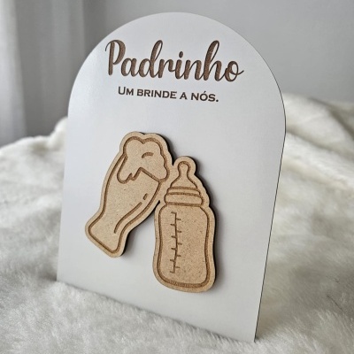 Expositor para prendas com mensagem para padrinho e ímanes de madeira de copo de cerveja e biberão sobre tecido branco.