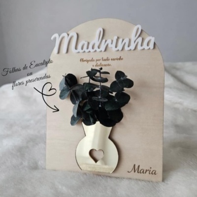 Placa decorativa de madeira com vaso dourado, folhas preservadas e texto para madrinha