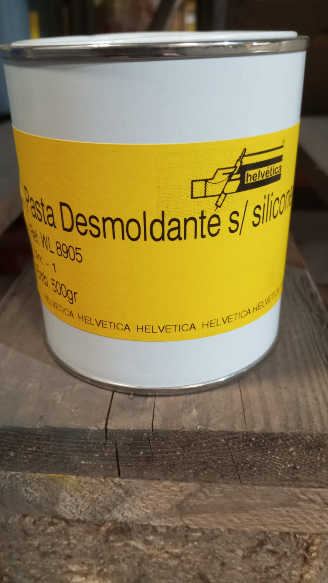 Frasco branco com rótulo amarelo de pasta desmoldante Helvetica sobre madeira