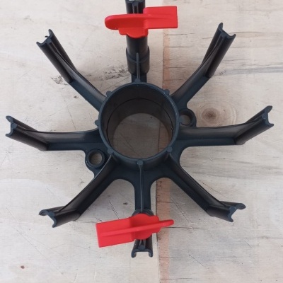 Peça plástica preta circular com braços e presilhas vermelhas sobre madeira clara