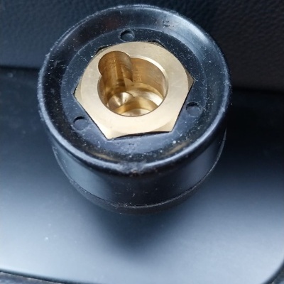 Adaptador cilíndrico preto com interior dourado sobre superfície preta texturada