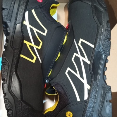 Par de sapatilhas pretas com detalhes amarelos e brancos dentro de caixa de cartão