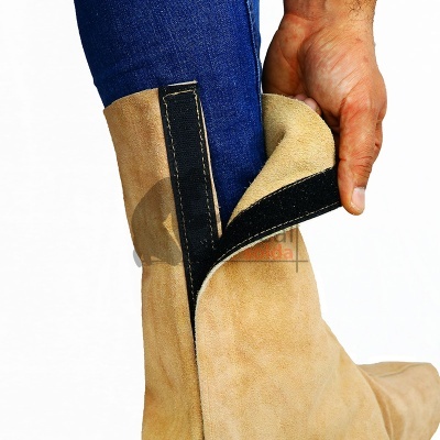 Bota bege de camurça com fecho de velcro preto sendo aberta por uma mão junto a jeans azul escuro